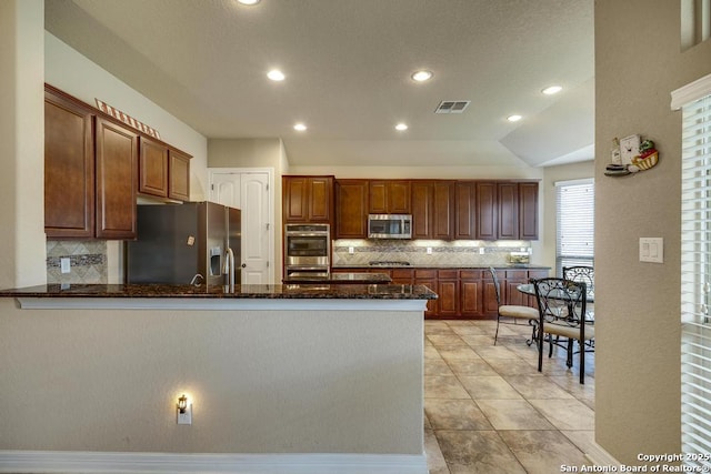 kitchen featuring stainless steel appliances, kitchen peninsula, decorative backsplash, and dark stone counters