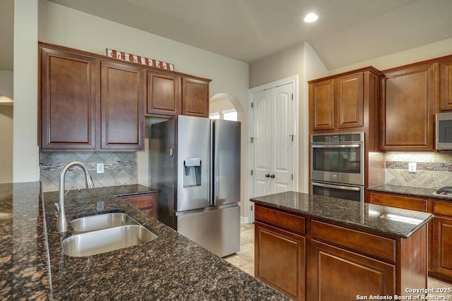 kitchen with appliances with stainless steel finishes, sink, dark stone countertops, backsplash, and light tile patterned floors