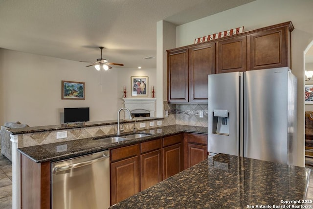 kitchen with ceiling fan, stainless steel appliances, a sink, decorative backsplash, and dark stone counters