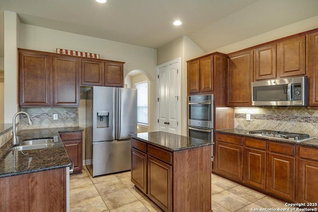 kitchen featuring arched walkways, stainless steel appliances, a sink, decorative backsplash, and dark stone counters