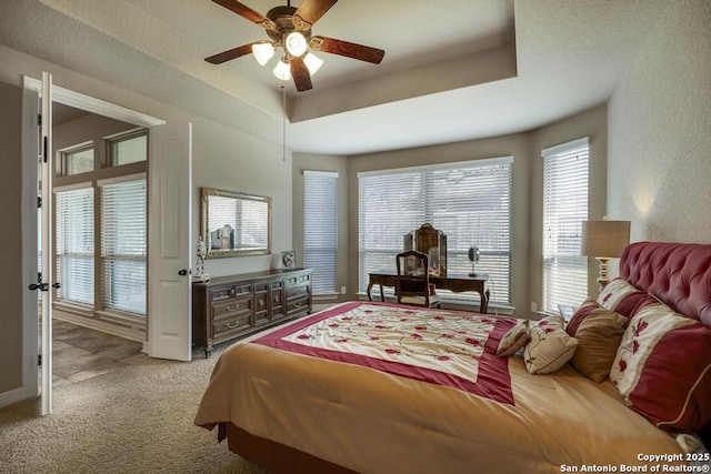 bedroom featuring light carpet, ceiling fan, and a tray ceiling