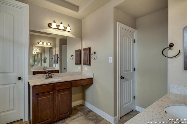 bathroom featuring two vanities, a sink, and baseboards