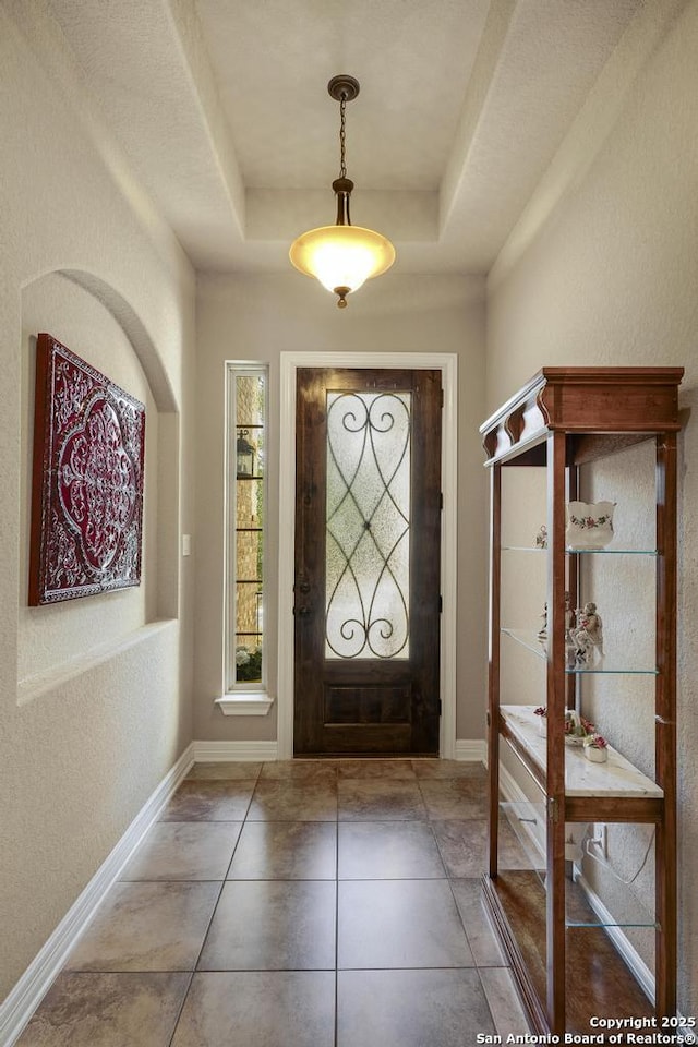 tiled entryway featuring a tray ceiling and baseboards