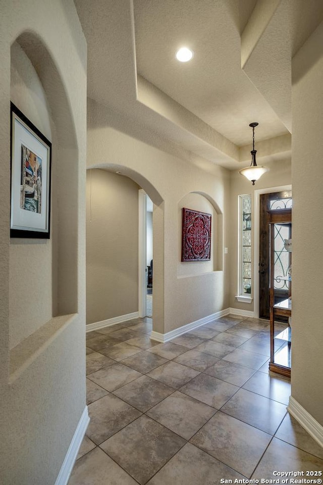 foyer featuring baseboards, a tray ceiling, and arched walkways