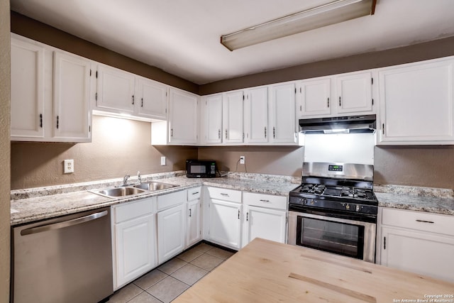 kitchen with light tile patterned flooring, appliances with stainless steel finishes, white cabinetry, sink, and light stone counters