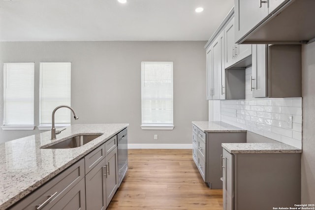 kitchen featuring sink, light stone counters, dishwasher, light hardwood / wood-style floors, and backsplash