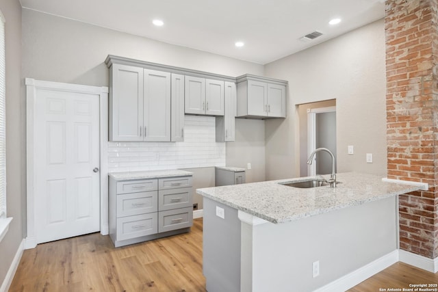 kitchen featuring sink, light hardwood / wood-style flooring, light stone countertops, and kitchen peninsula