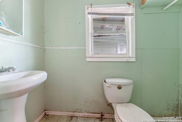 bathroom featuring toilet, sink, and tile walls