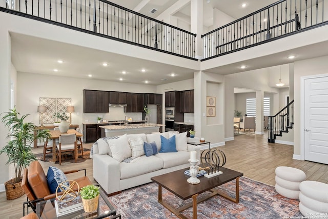 living room featuring a high ceiling, sink, and light hardwood / wood-style flooring