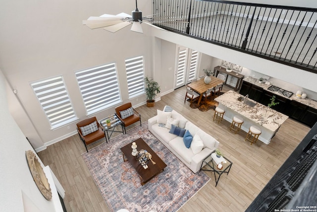 living room with a high ceiling, sink, ceiling fan, and light hardwood / wood-style flooring