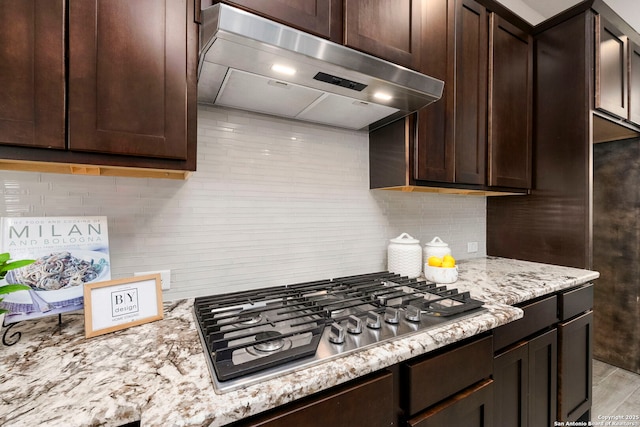 kitchen featuring light stone counters, dark brown cabinetry, stainless steel gas stovetop, and exhaust hood