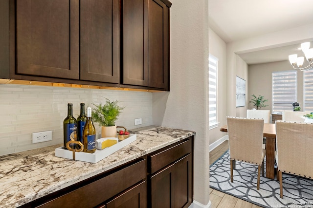 kitchen featuring dark brown cabinetry, light stone counters, tasteful backsplash, light hardwood / wood-style floors, and a chandelier