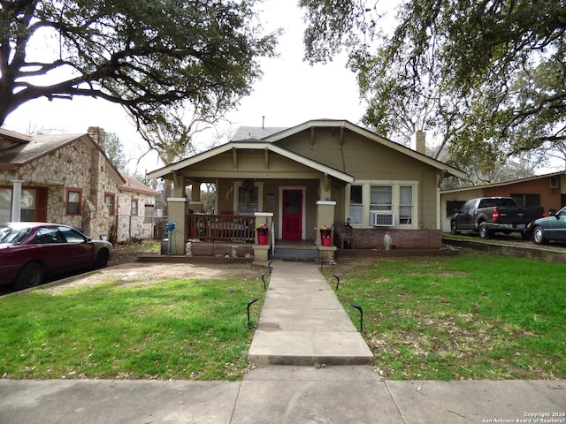 bungalow featuring cooling unit, covered porch, and a front lawn