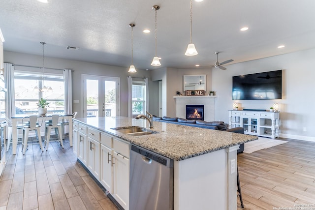 kitchen featuring decorative light fixtures, white cabinetry, dishwasher, sink, and a center island with sink