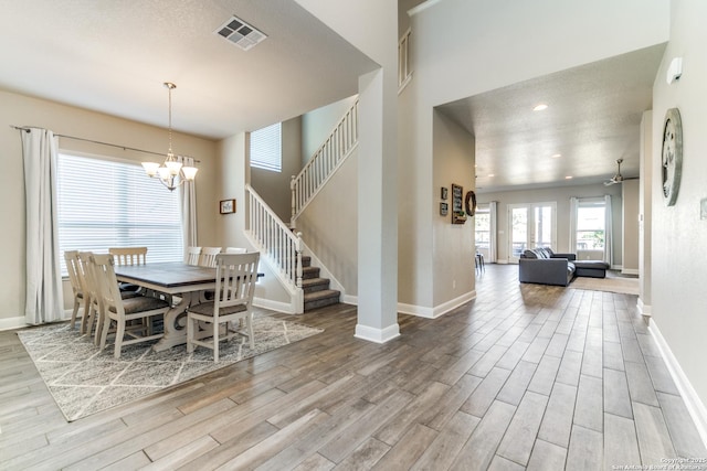 dining room featuring a towering ceiling, ceiling fan with notable chandelier, and light hardwood / wood-style floors