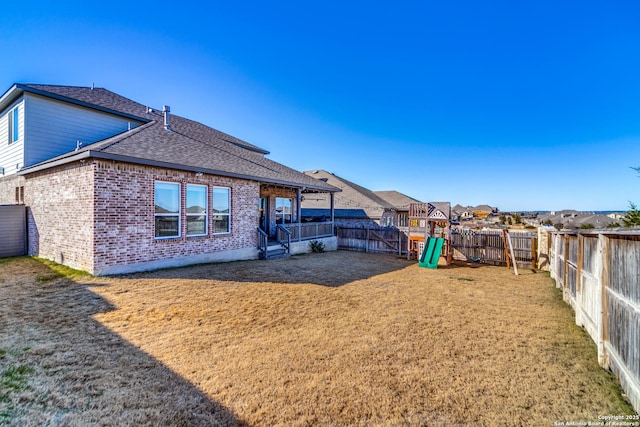 rear view of property featuring a playground and a yard