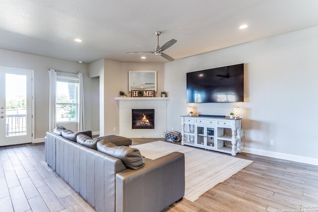 living room with ceiling fan, a brick fireplace, a textured ceiling, and light hardwood / wood-style floors