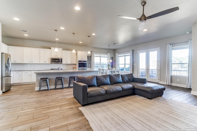 living room featuring french doors, ceiling fan, a textured ceiling, and light wood-type flooring