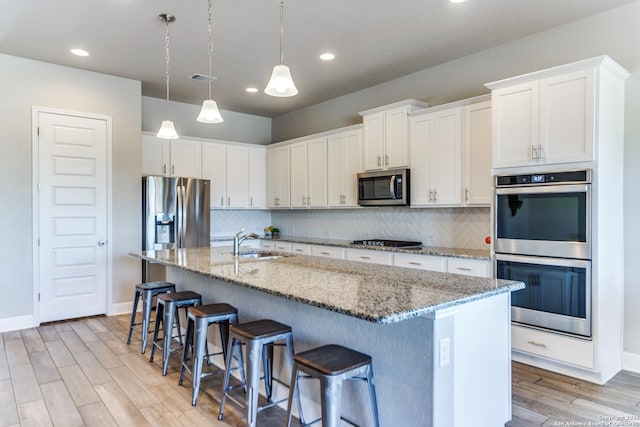 kitchen featuring sink, appliances with stainless steel finishes, a kitchen island with sink, a kitchen breakfast bar, and white cabinets