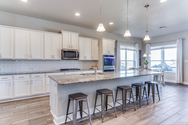 kitchen featuring sink, decorative light fixtures, stainless steel appliances, a kitchen island with sink, and white cabinets