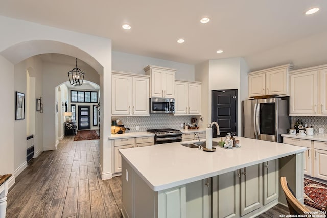 kitchen featuring dark wood-type flooring, sink, tasteful backsplash, stainless steel appliances, and a kitchen island with sink