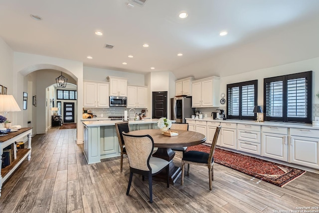 kitchen featuring tasteful backsplash, wood-type flooring, an island with sink, stainless steel appliances, and white cabinets