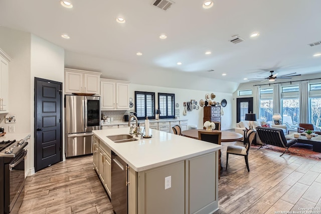 kitchen featuring appliances with stainless steel finishes, an island with sink, sink, decorative backsplash, and light wood-type flooring