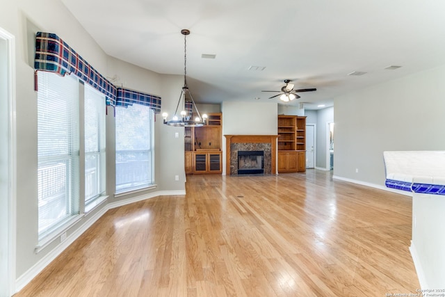 unfurnished living room featuring a tiled fireplace, wood-type flooring, and ceiling fan with notable chandelier