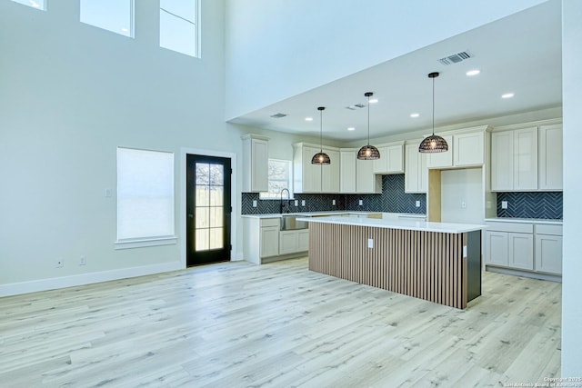 kitchen featuring sink, decorative light fixtures, light wood-type flooring, a kitchen island, and backsplash