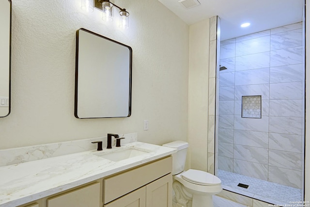 bathroom with vanity, tiled shower, and toilet