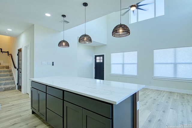 kitchen featuring a towering ceiling, decorative light fixtures, a center island, light stone counters, and light wood-type flooring