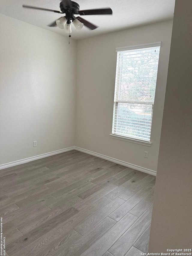 spare room with a ceiling fan, wood finished floors, a wealth of natural light, and baseboards