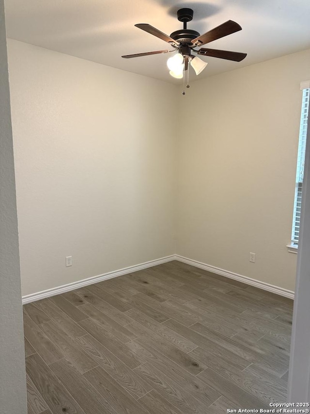 spare room featuring dark wood-style flooring, a ceiling fan, and baseboards