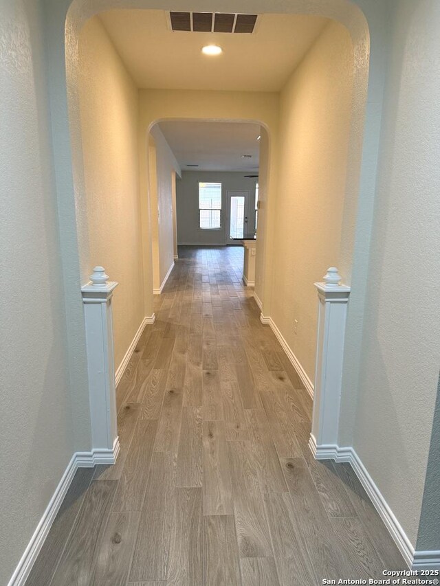 hallway featuring arched walkways, wood finished floors, visible vents, and baseboards