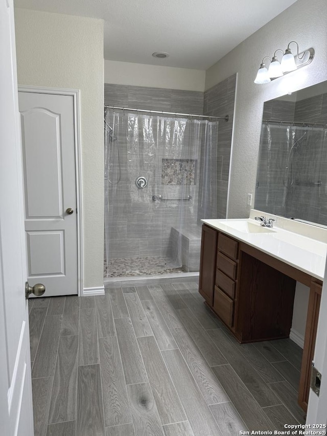 full bathroom featuring a textured wall, wood finish floors, a tile shower, and vanity