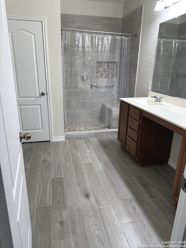 full bath featuring a textured wall, tiled shower, wood finish floors, and vanity