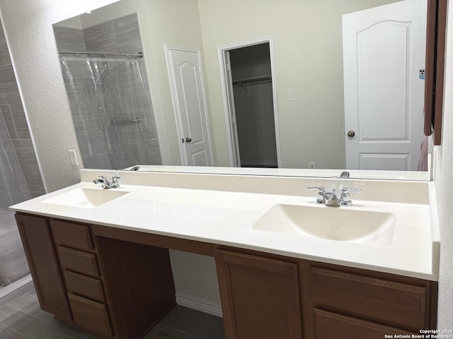 full bathroom featuring double vanity, tiled shower, a spacious closet, and a sink