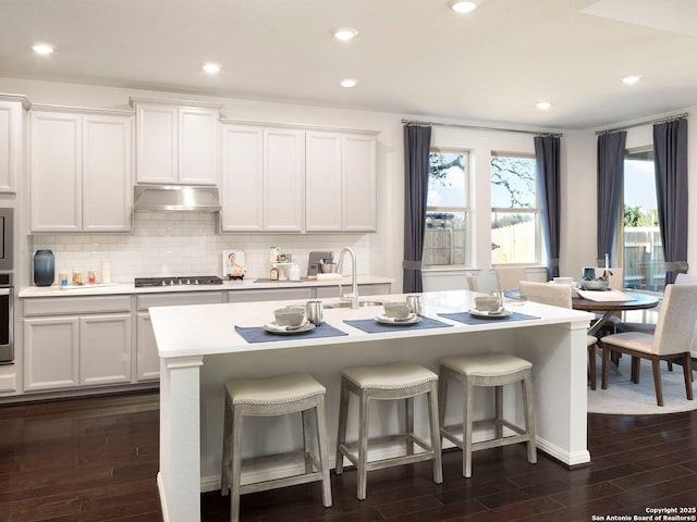 kitchen featuring white cabinetry, tasteful backsplash, dark hardwood / wood-style flooring, an island with sink, and stainless steel appliances