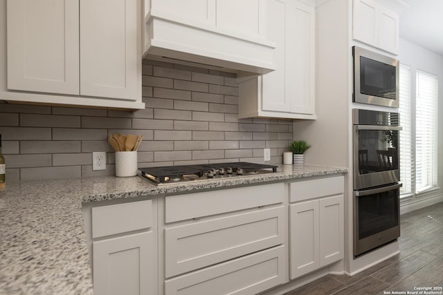 kitchen featuring premium range hood, tasteful backsplash, stainless steel appliances, light stone countertops, and white cabinets