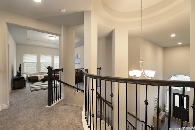 hallway with a tray ceiling, a chandelier, and carpet floors