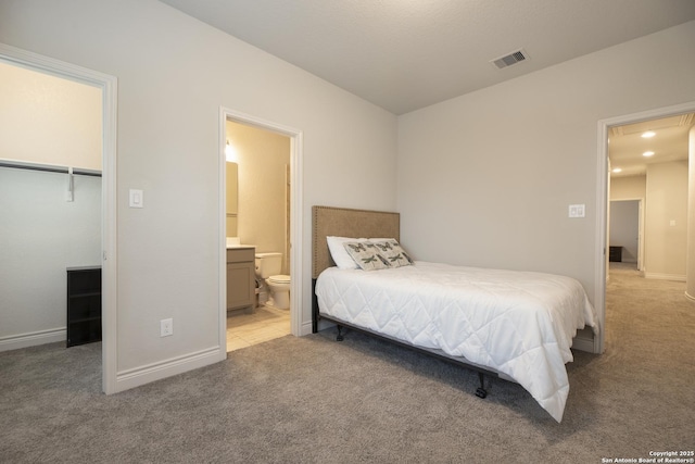 bedroom featuring a walk in closet, light carpet, ensuite bath, and a closet