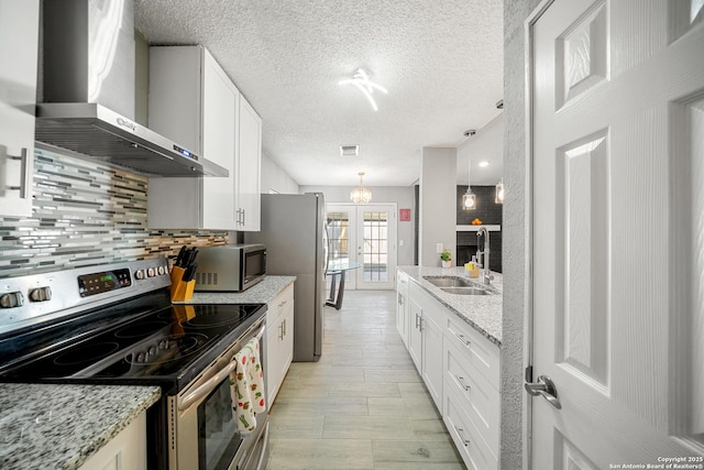 kitchen featuring appliances with stainless steel finishes, decorative light fixtures, sink, white cabinets, and wall chimney range hood