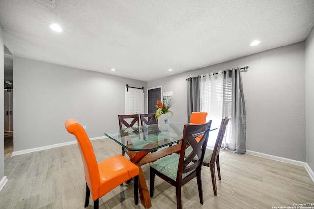 dining space with light hardwood / wood-style floors, a barn door, and a textured ceiling