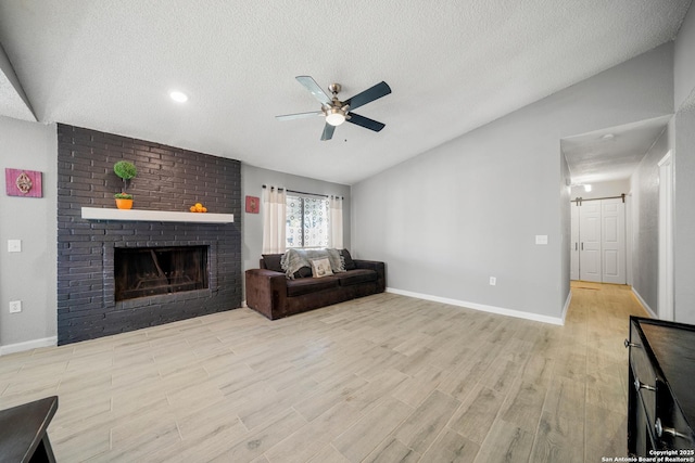 living room featuring lofted ceiling, a brick fireplace, a textured ceiling, ceiling fan, and light hardwood / wood-style floors