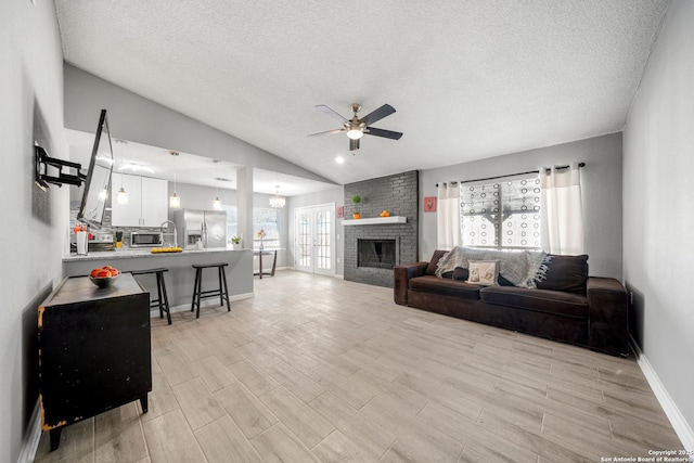 living room featuring lofted ceiling, a textured ceiling, light wood-type flooring, ceiling fan, and a fireplace