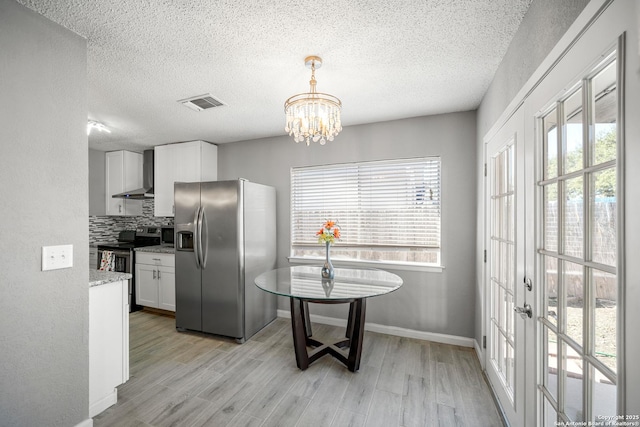 kitchen with appliances with stainless steel finishes, white cabinetry, hanging light fixtures, wall chimney exhaust hood, and light wood-type flooring