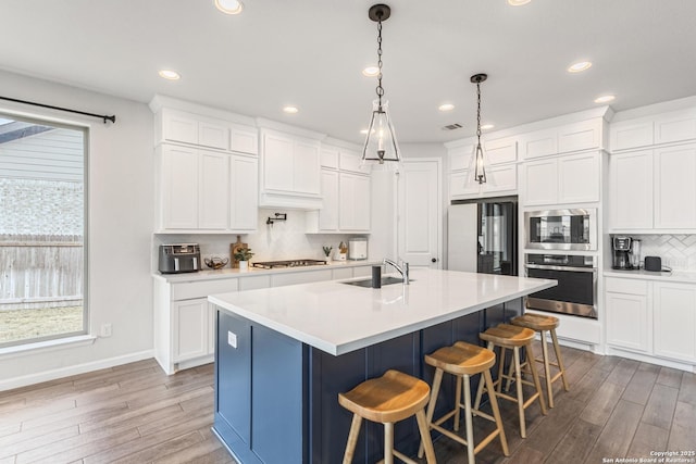 kitchen with appliances with stainless steel finishes, pendant lighting, sink, white cabinets, and a center island with sink