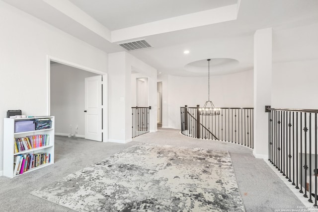 corridor featuring a notable chandelier, a tray ceiling, and carpet flooring