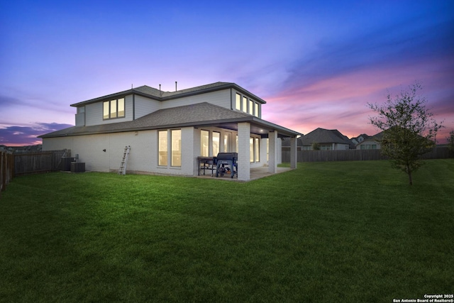 back house at dusk with a lawn, a patio, and central air condition unit