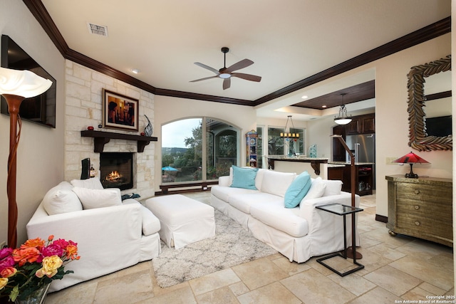 living room with ceiling fan, ornamental molding, a fireplace, and a tray ceiling